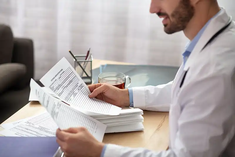 dark haired bearded doctor in a white robe looking at paperwork at injury clinic