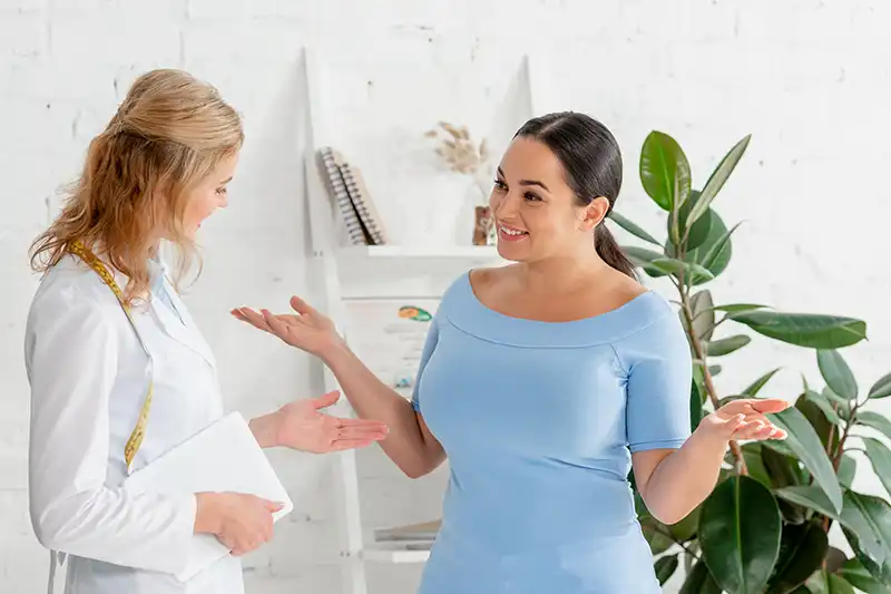 smiling nutritionist holding digital tablet and talking to patient about medically assisted weight loss